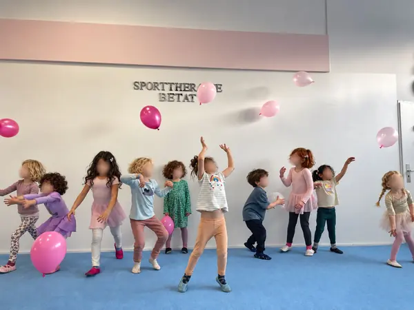 Kinder tanzen mit rosa Luftballons im Kursraum
