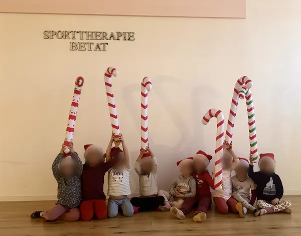 Kinder mit Weihnachtsmützen halten aufblasbare Zuckerstangen hoch